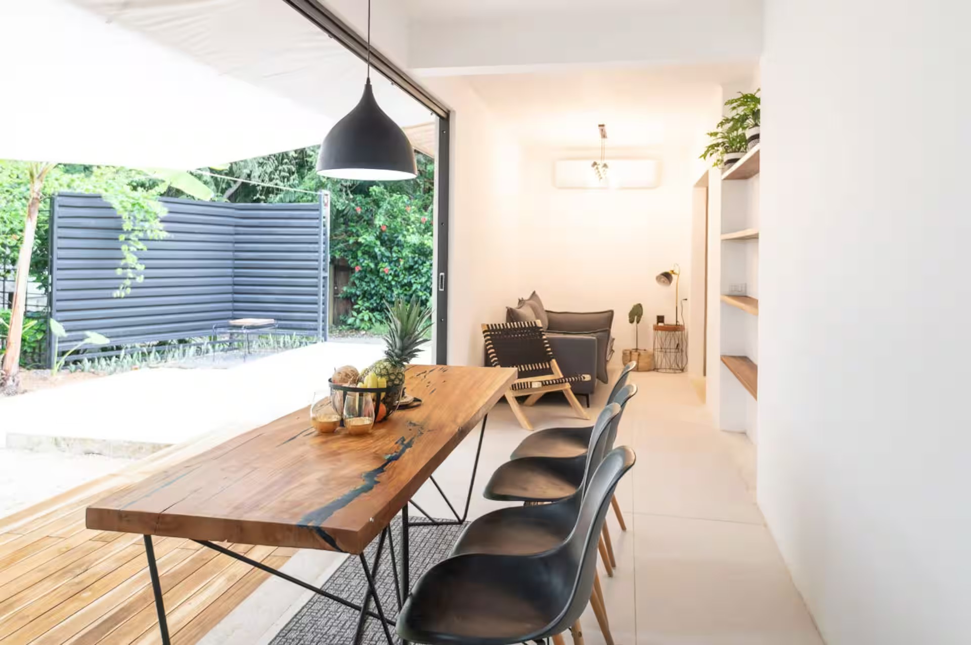 Dining and living area with tropical garden views, live-edge table, and black pendant lamp